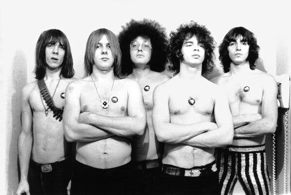 A black-and-white publicity photo of the MC5. They all have long hair and are shirtless, and they all have political buttons attached to their chests.