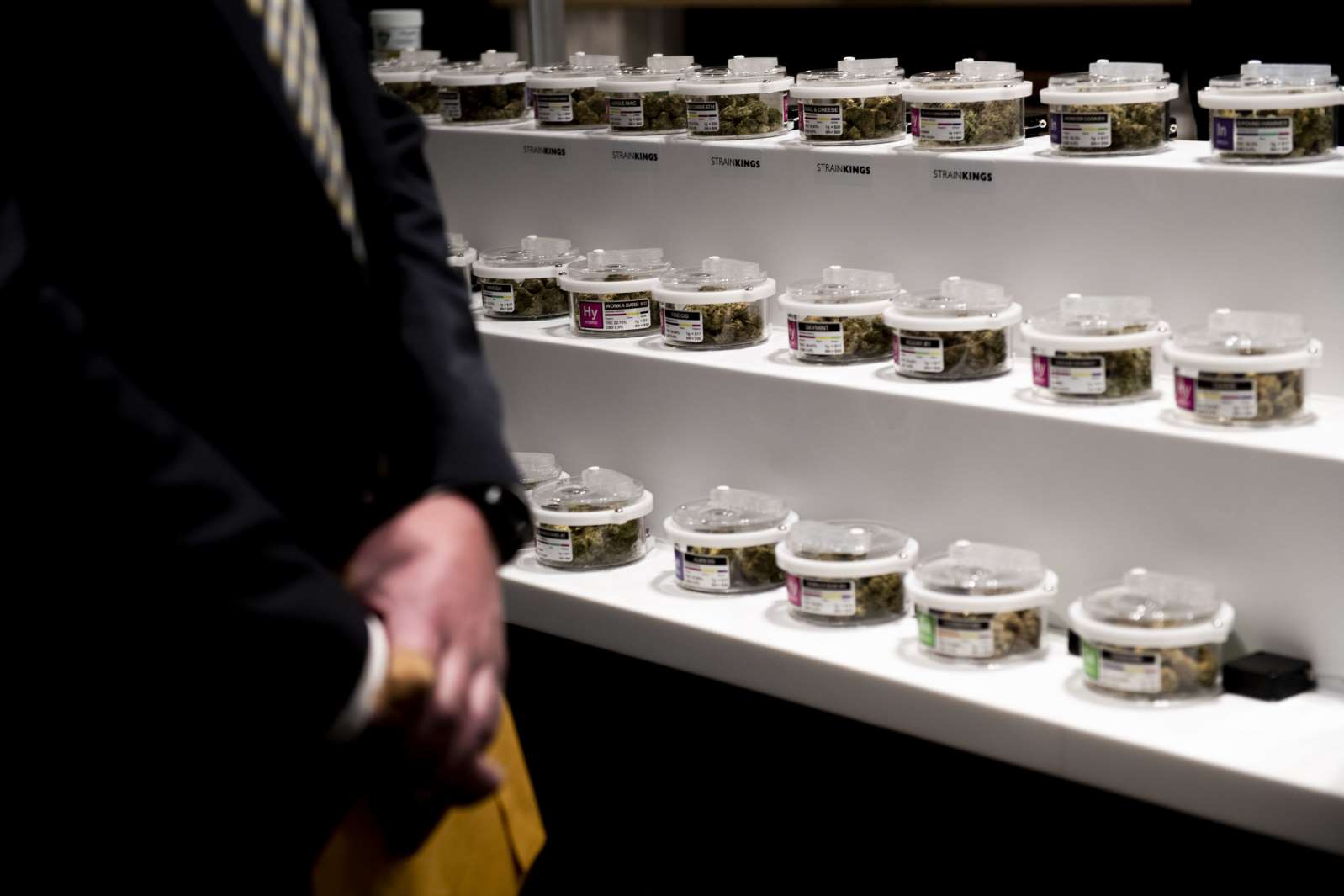a person standing in front of a counter: Containers of marijuana flowers sit on display as Exclusive Brands receives the first recreational marijuana license in the state of Michigan during a Marijuana Regulatory Agency press briefing on Tuesday Nov. 19, 2019 at 3820 Varsity Drive. Exclusive Brand will have their grand opening Friday and Saturday.