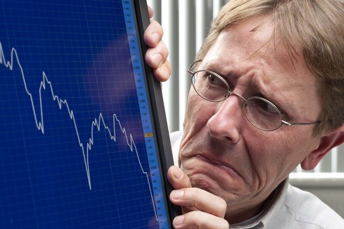 A visibly worried man looking at a plunging chart on his computer monitor. 