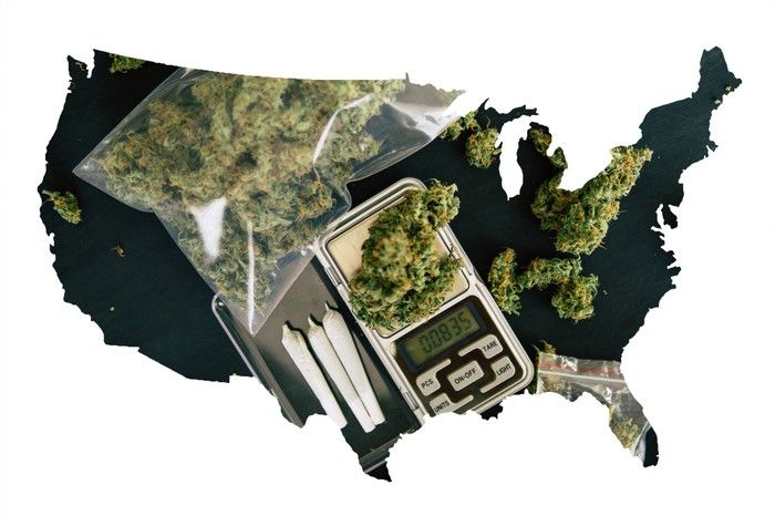 A black silhouette of the United States, partially filled in by baggies of cannabis, rolled joints, and a scale.