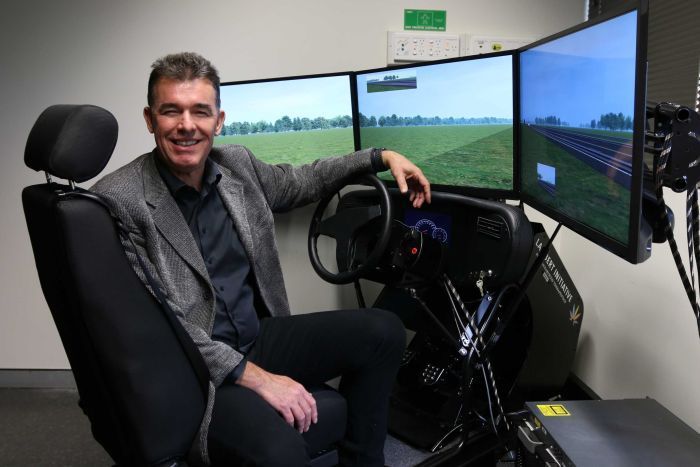 Professor Iain McGregor turns towards the camera from the seat of a driver simulation chair.