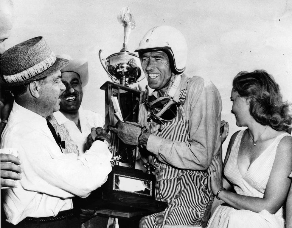 In this April 3, 1960 file photo, race car driver Carroll Shelby, center, of Dallas, receives his winner's trophy from promotion manager Dave Brandman, after winning the 200-mile International Grand Prix at the Riverside Raceways, in California. Shelby died on May 10, 2012, at a Dallas hospital.